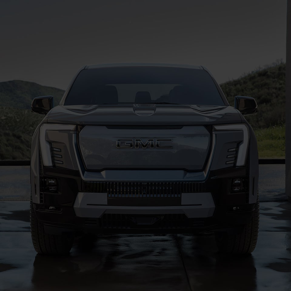 Front view of the 2025 GMC Sierra EV Denali parked outdoors on wet ground.